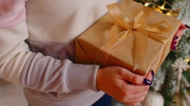 Elinde hediye kutusu tutan tanınmayan biri. Noel ağacının yanında elinde Noel hediyesi olan kadınların elleri. Kapatın. Tatillerde sürpriz kavramı.