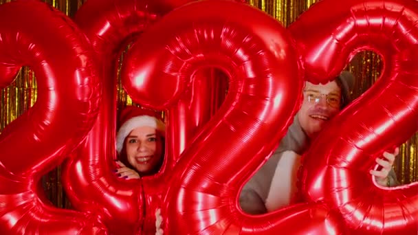 Nő és férfi, piros alakokkal, arany háttérrel. Boldog férfi és nő nézi a kamerát számokkal és mosollyal. Az ünnepek 2022-es megünneplésének koncepciója. Közelről.. — Stock videók