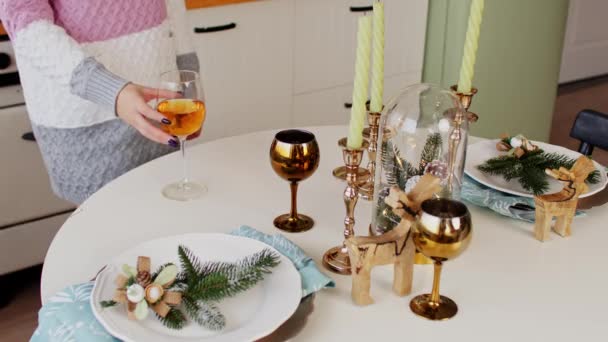 Świąteczny stół z kieliszkiem białego wina. Część ciała nierozpoznawalnej kobiety biorącej kieliszek wina i pijącej. Nieznana kobieta w długim swetrze z dzianiny świętująca Nowy Rok w kuchni. — Wideo stockowe