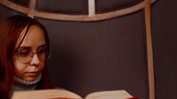 Young woman in glasses reading book. Interested student in eyeglasses reads book, preparing for educational lessons. Close up. — Stock Video
