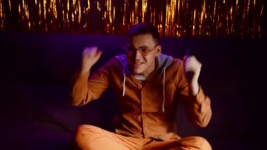 Uzaktan kumandalı genç adam kanepede oturuyor, televizyon seyrediyor ve karanlık odada parlak ışığı olan favori spor takımını destekliyor. Duygusal erkek spor kanalını izliyor ve kazandığı için seviniyor..