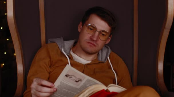 Joven con gafas leyendo libro. Estudiante interesado en anteojos lee libro, preparándose para lecciones educativas — Vídeo de stock