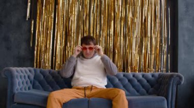 Acımasız adam turuncu gözlük takar ve kulaklı bir başlık takar, kanepeye oturur. Cesur erkek kameraya bakıyor ve arka planda altın süslemelerle poz veriyor..