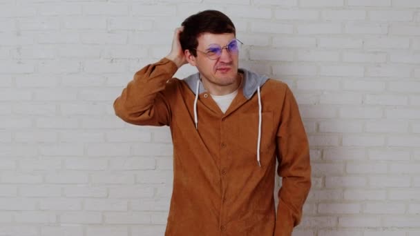 Nachdenklicher Mann mit Brille kratzt Kopf vor weißem Backsteinhintergrund. — Stockvideo