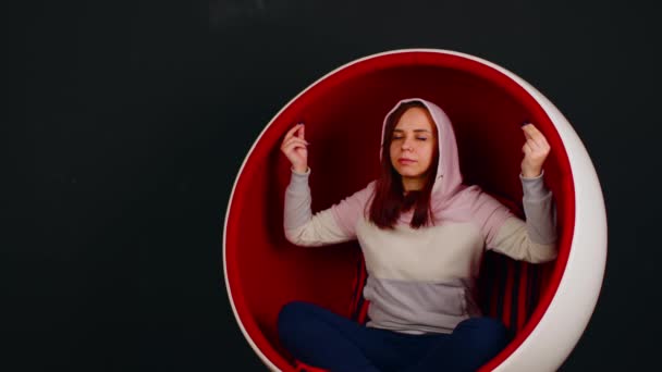 Young woman meditating in ball chair. Young female with closed eyes sitting in butterfly pose with zen gesture while practicing stress relief meditation in ball chair against black background — Stock Video