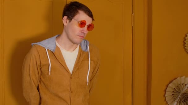 Mladý pohledný muž v brýlích, stojící na pozadí hnědých dveří v místnosti. Portrét stylového muže dívajícího se stranou. — Stock video