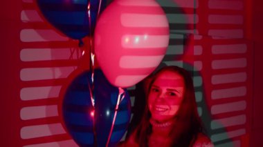 Koyu kırmızı stüdyoda balonlu bir kadın. Süveter giymiş, balonlu bir kadın. Kutlama için kırmızı ışıklı bir odada.