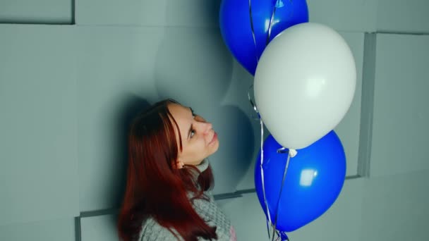 Jonge vrouw met luchtballonnen bij de muur. Portret van een lachende vrouw die naar ballonnen in de kamer kijkt. — Stockvideo