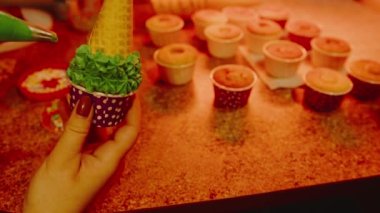 Tanınmayan bir kadın elinde waffle külahlı küçük bir kek tutuyor. Bilinmeyen kadın waffle külahını yeşil kremayla süslüyor. Ev yapımı kremalı ilginç kekler hazırlayan kadınların ellerini kapat..