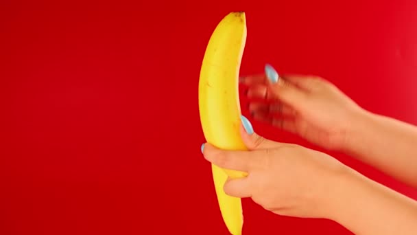 Жінки руки чистять банан на червоному тлі. Нерозпізнана людина чистить фрукти від шкірки . — стокове відео
