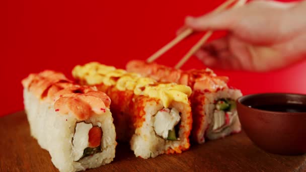 Pessoa a comer sushi com pauzinhos. Crop pessoa anônima com pauzinhos comendo vários tipos de rolos de sushi em um fundo vermelho. — Vídeo de Stock