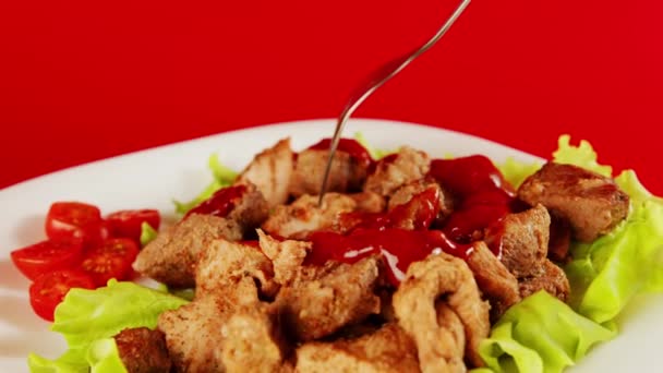 Een mensenhand met een vork dompelt een stuk vlees in ketchup op een rode achtergrond. Close-up van een vrouw handen met behulp van een bestek, het eten van vlees overvloedig gegoten met rode saus — Stockvideo