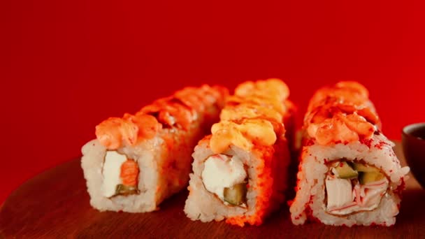 Sushi rolls near soy sauce. Set of tasty sushi rolls with cheese topped with sauce served on wooden table against red background in light room — Αρχείο Βίντεο