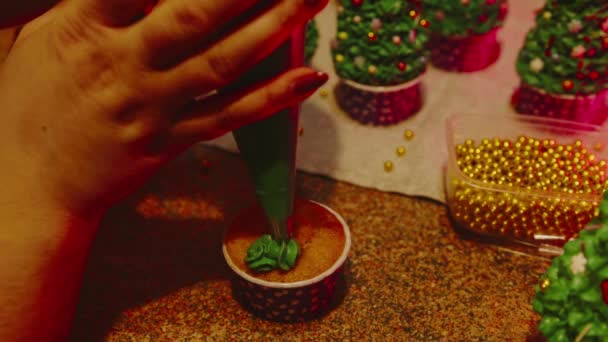 Small cupcake on table. Unrecognizable woman decorates cupcake with green cream. Close up of womans hands decorating cake with custard. — Stock Video