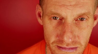 Portrait of forty-year-old man with unshaven and wrinkled face on red background. Mature male looking at camera.