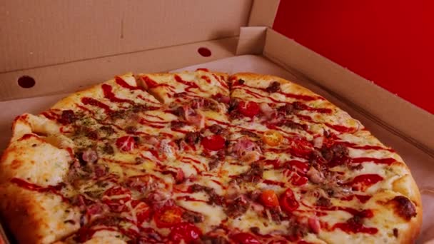 Großaufnahme einer großen Pizza in Karton auf rotem Hintergrund. Appetitliche Pizza mit verschiedenen Zutaten — Stockvideo