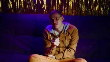 Uzaktan kumandalı üzgün adam kanepeye oturur ve parıldayan ışıkla karanlık odada televizyon izler. Gözlüklü tatminsiz erkek gece geç saatlerde televizyon izleyerek kanal değiştiriyor.