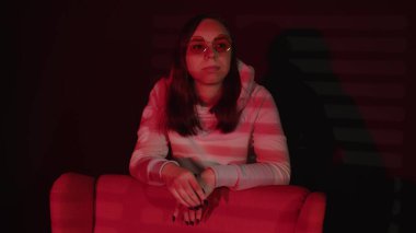 Koltuğa yaslanan düşünceli bir kadın. Sıcak kapüşonlu ve gözlüklü uzun saçlı düşünceli genç bayan koltuğa yaslanıyor ve rüya gibi gözlerini kaçırıyor..