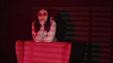 Koltuğa yaslanan düşünceli bir kadın. Sıcak kapüşonlu ve gözlüklü uzun saçlı düşünceli genç bayan koltuğa yaslanıyor ve rüya gibi gözlerini kaçırıyor..