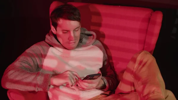 Νεαρός Άνδρας Περιήγηση Smartphone Κάθεται Στην Πολυθρόνα Σκοτεινό Δωμάτιο Κόκκινο — Φωτογραφία Αρχείου