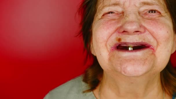 Mulher madura em fundo vermelho. Retrato da avó rindo com um dente na boca. Conceito de alterações relacionadas com a idade. — Vídeo de Stock