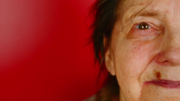 Del av äldre kvinnor ansikte på röd bakgrund med utrymme för text. Gammal kvinna ler och tittar på kameran. — Stockvideo