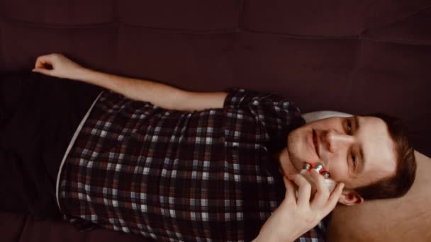 Jovem sorrindo homem usando massageador 3d para rosto. Homem relaxado deitado no sofá e usando massageador elétrico. Conceito de tratamento de beleza em casa. — Vídeo de Stock