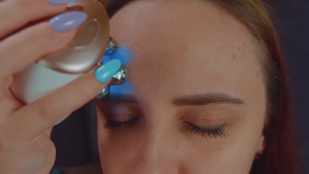 Une femme à la peau problématique utilisant un masseur électrique pour le visage. Femme utilisant un masseur électrique sur le visage tout en se relaxant sur le canapé et en faisant une procédure de beauté à la maison. Concept de contrôle de l'acné — Video