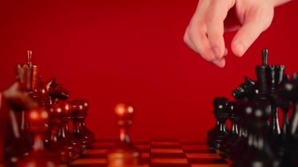 Primo piano di scacchi in legno bianco e nero a bordo. La mano di Mans fa la mossa di pedone nero su scacchiera su uno sfondo rosso. Concetto di gioco intelligente, logico e strategico. — Video Stock