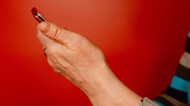 Äldre kvinnor hand med mobiltelefon på röd bakgrund. Oigenkännlig mogen kvinna håller smartphone. Närbild. — Stockvideo