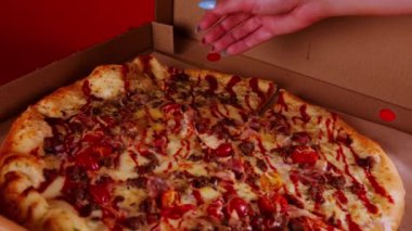Kırmızı arka planda büyük boy pizza. Kadın eli bir dilim pizza alır. Yavaş çekim.