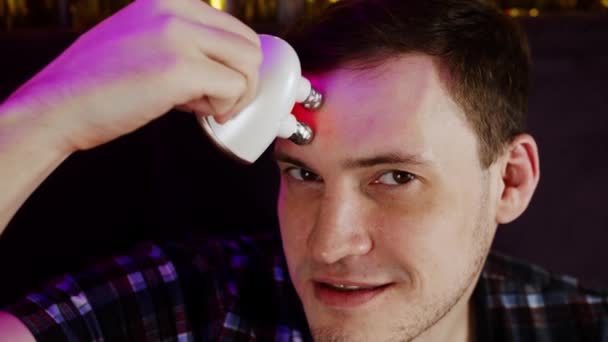 Junger Mann mit 3D-Massagegerät für Gesicht. Entspannter Mann genießt elektrische Massage auf der Stirn gegen Falten. Konzept der Männerpflege und Schönheitsbehandlung zu Hause. Nahaufnahme. — Stockvideo