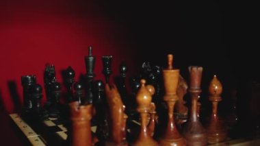 Alacakaranlıkta kırmızı arka planda dönen tahta satranç taşları. Tahta şekilli satranç oyunu. Masa oyunu ve boş zaman etkinliği kavramı.