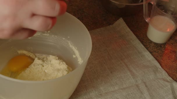 Felismerhetetlen személy tojást ad a tésztához tálba, és keverővel habverőt készít. Ismeretlen háziasszony készíti a megvert tésztát. Közelről. A házi sütéshez való tésztakészítés fogalma. — Stock videók