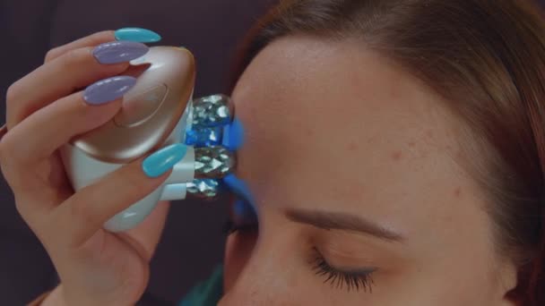 Kobieta z problematyczną skórą używająca elektrycznego masażu twarzy. Kobieta korzystająca z elektrycznego masażera na twarzy podczas relaksu na sofie i wykonywania zabiegów kosmetycznych w domu. Koncepcja kontroli trądziku — Wideo stockowe
