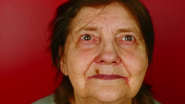 Mature woman on red background. Portrait of grandmother looking around and smiling. — Stock Video