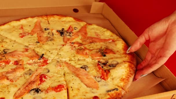 Apetyczna duża pizza w pudełku na czerwonym tle. Kobieca ręka bierze kawałek pizzy. Zwolniony ruch. — Wideo stockowe