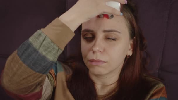En avslappnad kvinna som använder ansiktsmassage. Kvinna med elektrisk massage i ansiktet samtidigt som du kopplar av på soffan och gör skönhetsingrepp hemma. Begreppet skönhetssalong hemma — Stockvideo
