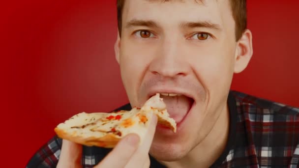 Mladý muž jí pizzu. Šťastný samec těší plátek pizzy na červeném pozadí. — Stock video