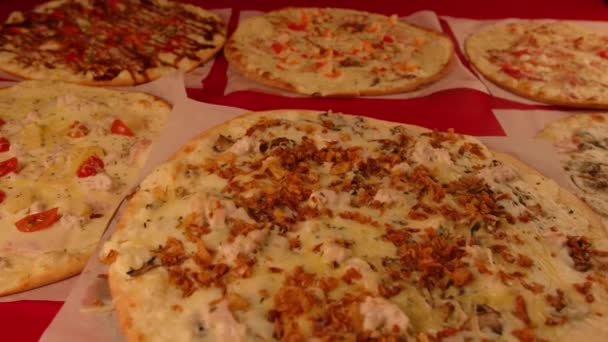 Apetitiva pizza pequeña girando sobre el fondo de otras pizzas. Deliciosa pizza con diferentes ingredientes. Concepto de fiesta, comida rápida y comida para llevar. — Vídeo de stock