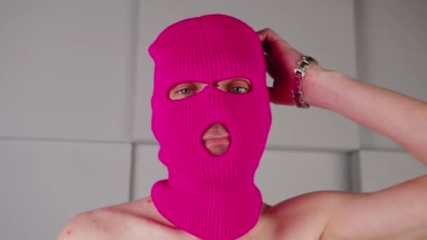 Портрет вдумчивого неузнаваемого человека в розовой балаклаве. Хулиган в маске смотрит в камеру и чешет голову. — стоковое видео