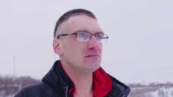 Ein erwachsener Mann mit Brille blickt nachdenklich in die Ferne, steht im Winter bei schneebedecktem Wetter auf der Straße. Erwachsener Mann in Unterwäsche und Brille — Stockvideo