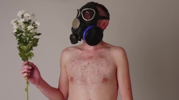 Faceless shirtless man in gas mask smelling flowers. Unrecognizable male with naked torso in black gas mask smelling bouquet of fresh white flowers near gray wall — Stock Video