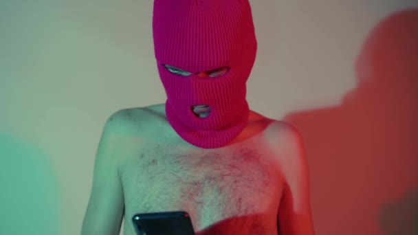 Anonym skjorta man i Balaclava surfa smartphone. Sidovy av farlig oigenkännlig hane med naken bål i balaklava SMS på modern mobiltelefon när du står i neonljus — Stockvideo