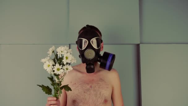 Um homem sem rosto sem camisa com uma máscara de gás com flores. Um homem irreconhecível com um tronco nu em uma máscara de gás preto com um buquê de flores brancas frescas. Conceito: alergia e poluição ambiental — Vídeo de Stock