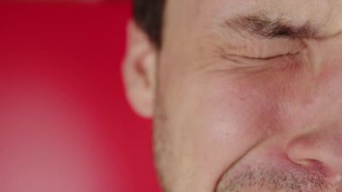 Kırmızı arka planda ağlayan bir adamın portresi. Traşsız bir adam ağlıyor ve yas tutuyor.