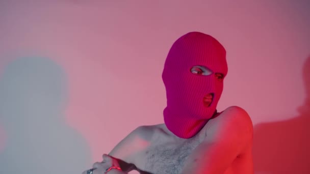Anonymous shirtless man in balaclava scratching hand. Unrecognizable male with naked torso wearing pink balaclava scratching shoulder and looking away while standing near wall. — Stock Video