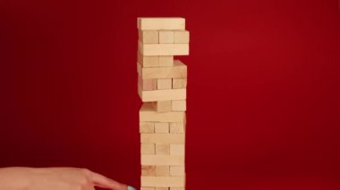 Kırmızı arka planda Jenga oyunu. Kadınların eli küçük tahta blokları söker. Masa oyunu oynayan tanınmayan kişi Jenga. Evde boş zaman aktivitesi kavramı.