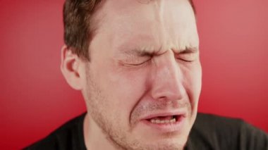 Kırmızı arka planda ağlayan bir adamın portresi. Traşsız bir adam ağlıyor ve yas tutuyor.