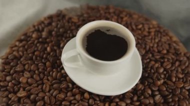 Kahve fincanı ve kahve fincanı, etrafa saçılmış buharlı. Kavrulmuş fasulyeli taze kahve ve dumanlı kahve kompozisyonu. Hazırlık kokulu içecek konsepti.